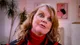 Cathy Fisher in a red polo neck and a red and black patterned jacket, in front of her paintings, mid-sentence