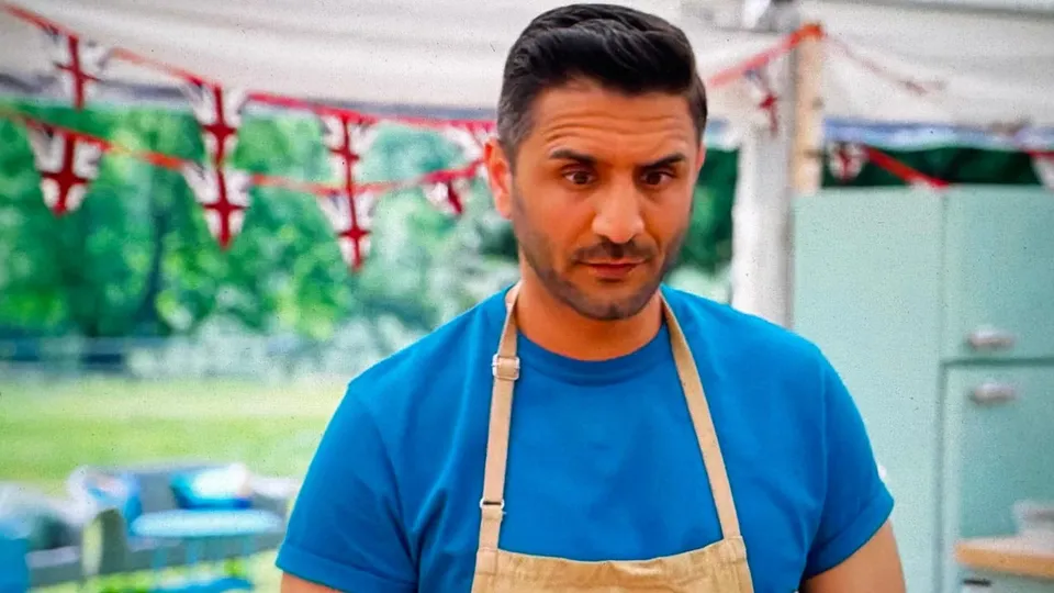 Chigs Parmar in the tent in a blue T-shirt and apron, under Union Jack bunting, glancing down