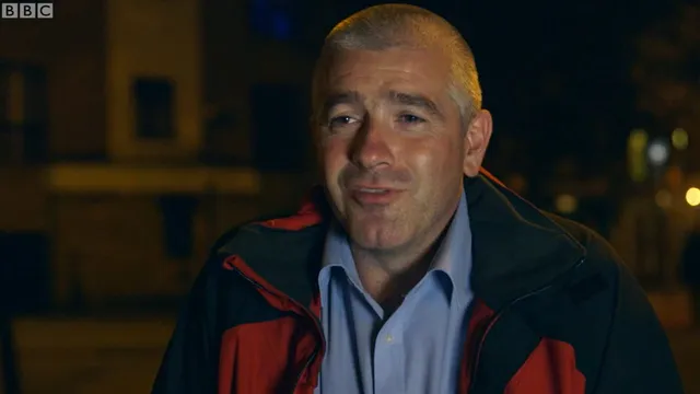 David outside at night in a red and black jacket over a blue shirt, mid-sentence