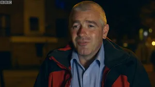 David outside at night in a red and black jacket over a blue shirt, mid-sentence
