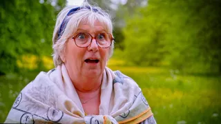 Dawn Hollyoak outside the tent in a patterned shawl and a blue headscarf, eyes wide and mouth open, stunned