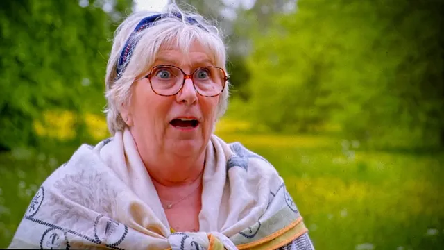 Dawn Hollyoak outside the tent in a patterned shawl and a blue headscarf, eyes wide and mouth open, stunned