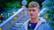 Jamie Finn outside the tent in a denim jacket with a fleece collar, by stone steps strung with fairy lights