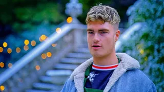 Jamie Finn outside the tent in a denim jacket with a fleece collar, by stone steps strung with fairy lights