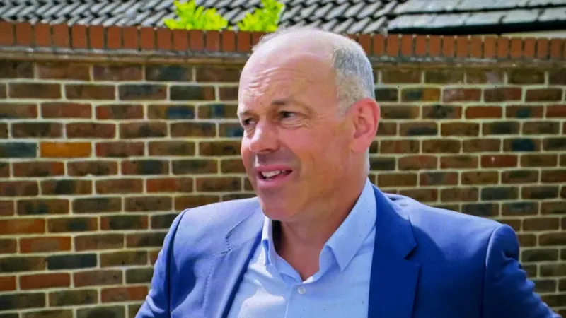 Phil Spencer in a blue jacket and open-necked shirt in front of a brick wall, mid-sentence, a few seconds after the chuff
