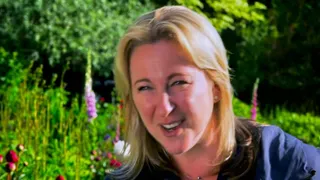 Stacey Hart in a garden of foxgloves, mid-sentence, smiling as she talks to camera