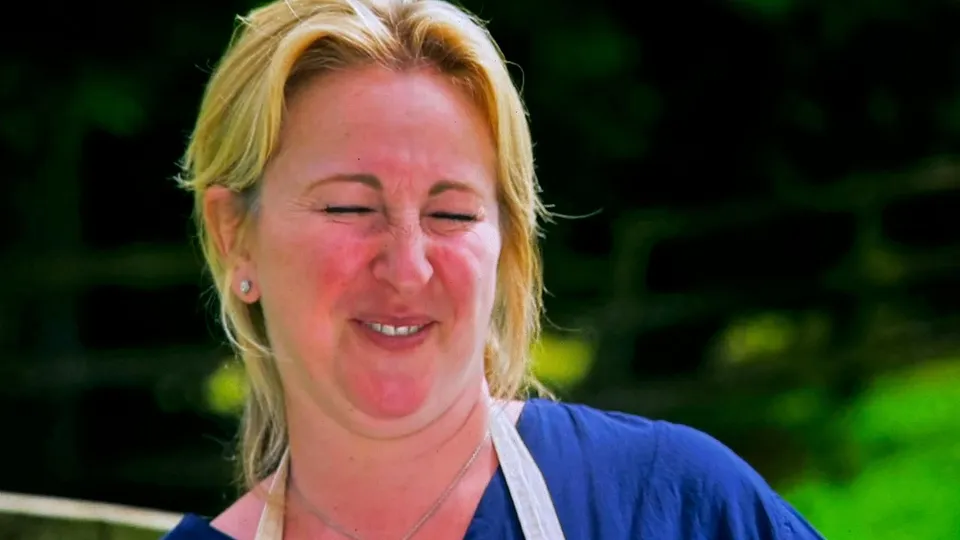 Stacey Hart outside the tent, eyes screwed shut, beaming, in a blue top and the show's apron