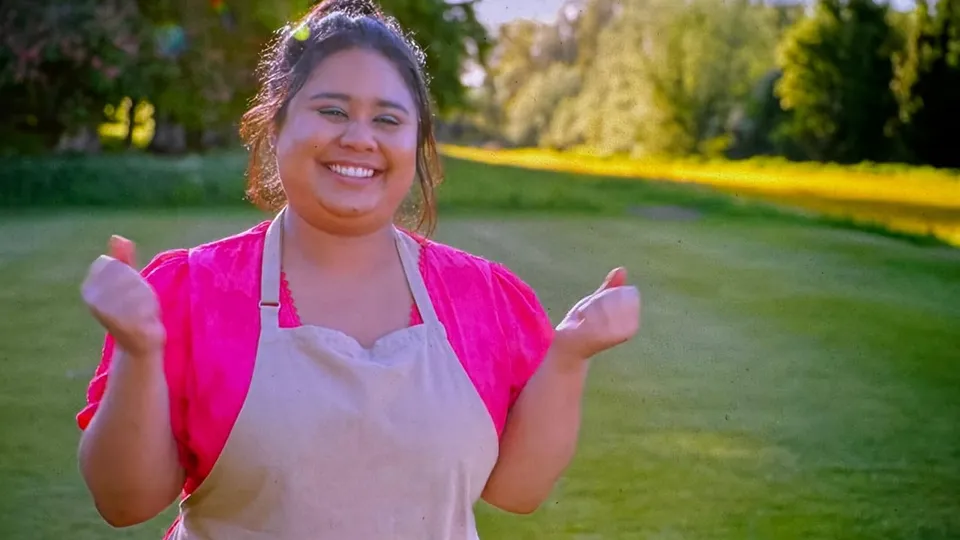 Syabira Yusoff on the lawn outside the tent in a pink top and apron, beaming, both fists raised