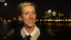 Tamara outside at night by the river, the City lights and a full moon behind her, smiling