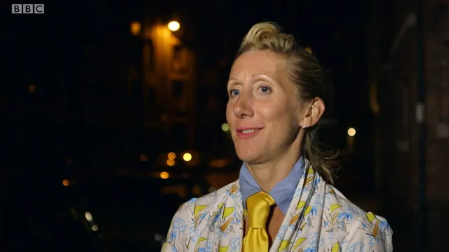 Tamara outside at night in a patterned jacket, blue collar and yellow tie, smiling
