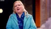 Tracey outside in a turquoise parka and a blue scarf, looking up and smiling, mid-sentence