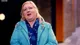 Tracey outside in a turquoise parka and a blue scarf, looking up and smiling, mid-sentence